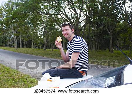 Man eating sandwich on trunk of car View Large Photo Image Picture - Man eating sandwich on trunk of car. Fotosearch