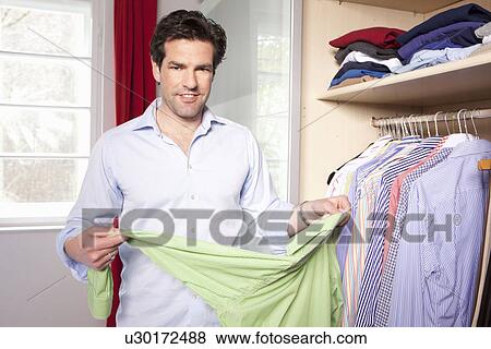 Man hanging up clothes in closet View Large Photo Image Stock Photo - Man hanging up clothes in closet. Fotosearch