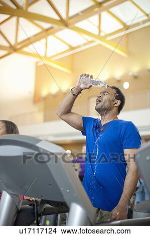 Picture - Man pouring water on himself in gym. Fotosearch