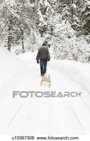 Stock Photo - Man pulling sled in snowy field. Fotosearch