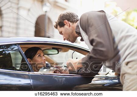Stock Image - Man talking to woman through car window. Fotosearch