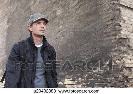 Stock Image - Man walking by concrete wall. Fotosearch