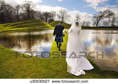 Newlywed couple walking on grassy bridge View Large Photo Image Stock Photo - Newlywed couple walking on grassy bridge. Fotosearch
