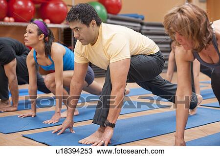 Stock Image - People practicing yoga in studio. Fotosearch