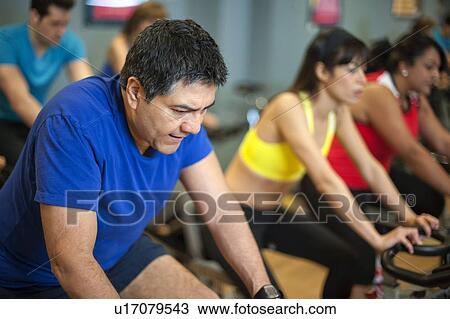 Stock Image - People using spin machines in gym. Fotosearch