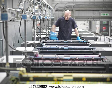 Stock Image - Printer inking printing press in shop. Fotosearch