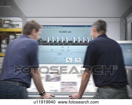 Stock Image - Printers examining printing press. Fotosearch