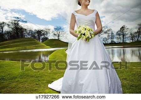 Stock Photograph - Smiling bride walking in field. Fotosearch