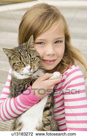 Stock Image - Smiling girl holding cat outdoors. Fotosearch