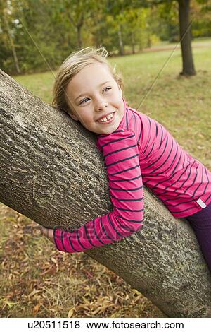 Stock Photo - Smiling girl hugging tree outdoors. Fotosearch
