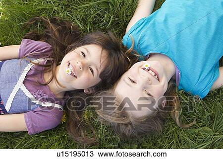 Stock Image - Smiling girls laying in grass together. Fotosearch