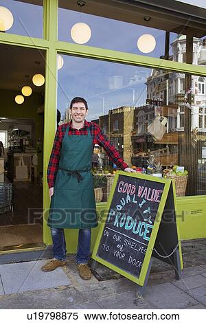 Stock Photography - Smiling grocer standing outside store. Fotosearch
