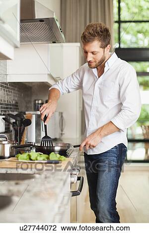 Stock Image - Smiling man cooking in kitchen. Fotosearch