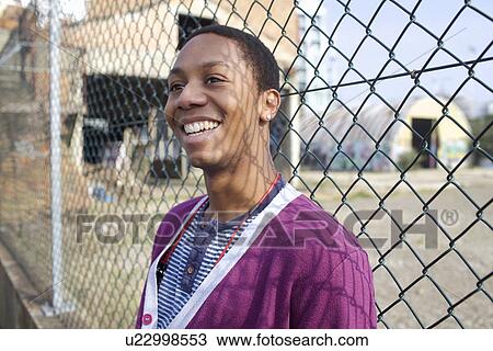 Stock Image - Smiling man leaning against fence. Fotosearch