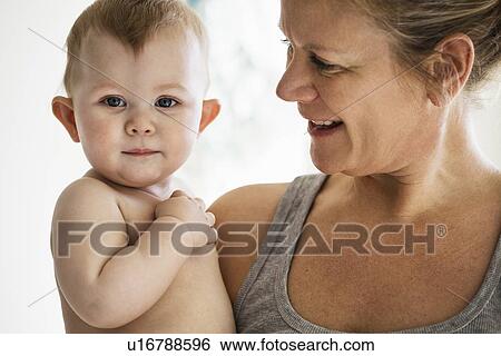 Smiling mother holding baby girl View Large Photo Image Stock Photograph - Smiling mother holding baby girl. Fotosearch