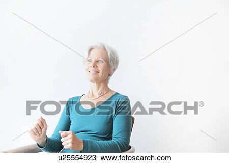 Stock Image - Smiling older woman sitting in chair. Fotosearch
