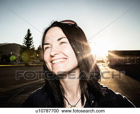 Stock Image - Smiling woman and sun flare outdoors. Fotosearch