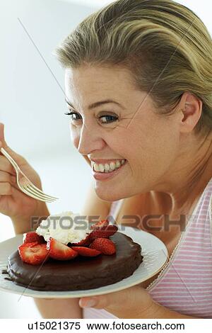 Stock Photography - Smiling woman eating cake in kitchen. Fotosearch