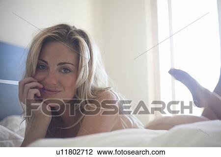 Stock Image - Smiling woman laying on bed. Fotosearch