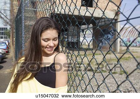 Stock Image - Smiling woman leaning against fence. Fotosearch