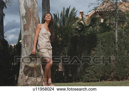 Smiling woman leaning against tree View Large Photo Image Picture - Smiling woman leaning against tree. Fotosearch