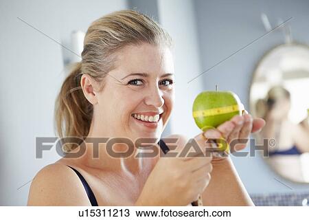 Stock Image - Smiling woman measuring apple. Fotosearch