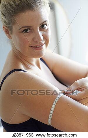 Stock Image - Smiling woman measuring her arm. Fotosearch