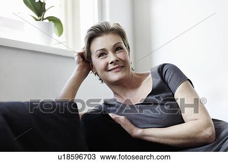 Smiling woman sitting on sofa View Large Photo Image Stock Image - Smiling woman sitting on sofa. Fotosearch