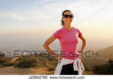 Stock Image - Smiling woman standing on hilltop. Fotosearch