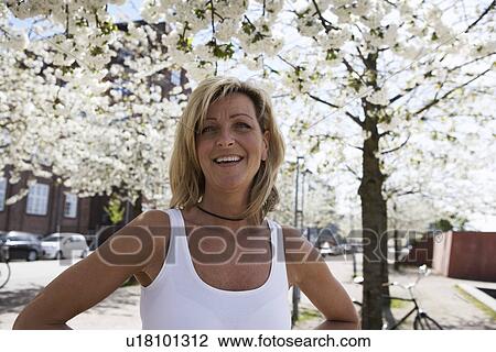 Smiling woman standing under tree View Large Photo Image Stock Image - Smiling woman standing under tree. Fotosearch