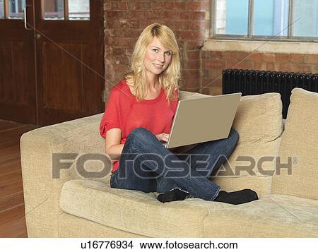 Picture - Smiling woman using laptop on sofa. Fotosearch