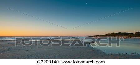 Stock Image - Sun rising over sandy beach. Fotosearch
