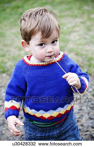 Stock Image - Toddler boy chewing on stick outdoors. Fotosearch