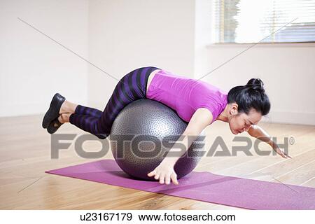 Stock Photo - Woman balancing on ball in yoga studio. Fotosearch