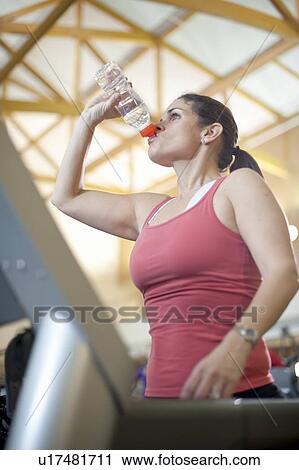 Stock Image - Woman drinking water bottle in gym. Fotosearch