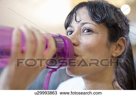 Stock Image - Woman drinking water bottle in gym. Fotosearch