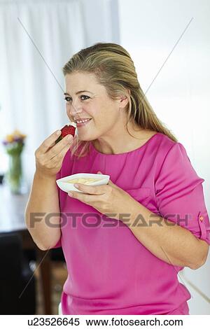 Stock Photography - Woman eating strawberry and cream. Fotosearch