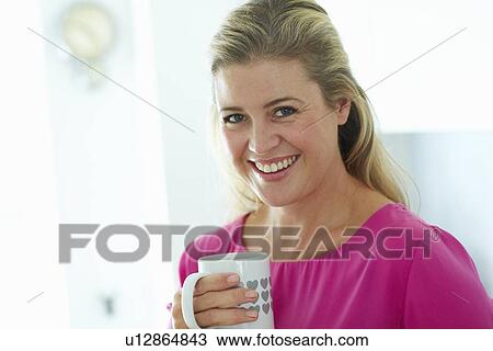 Stock Image - Woman having cup of coffee in kitchen. Fotosearch