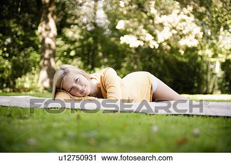 Stock Image - Woman laying on blanket in park. Fotosearch