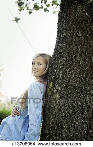 Picture - Woman leaning against tree outdoors. Fotosearch