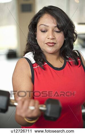 Stock Image - Woman lifting weights in gym. Fotosearch