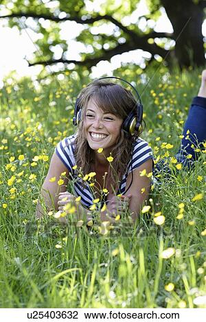 Stock Image - Woman listening to headphones in grass. Fotosearch
