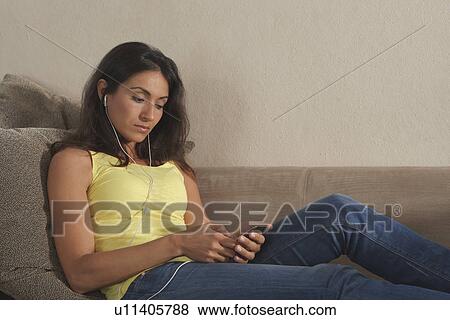 Stock Photo - Woman listening to headphones on sofa. Fotosearch