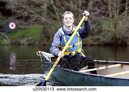 Stock Image - Woman rowing canoe on still lake. Fotosearch