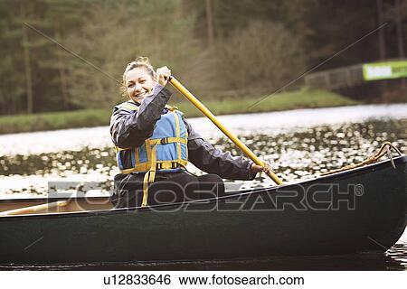 Stock Photograph - Woman rowing canoe on still lake. Fotosearch