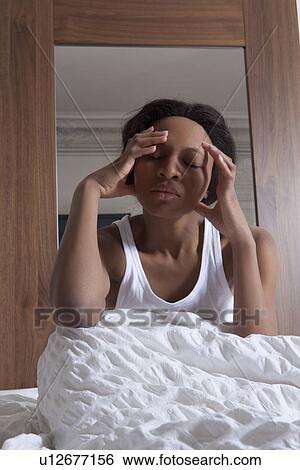 Stock Photograph - Woman rubbing her temples in bed. Fotosearch