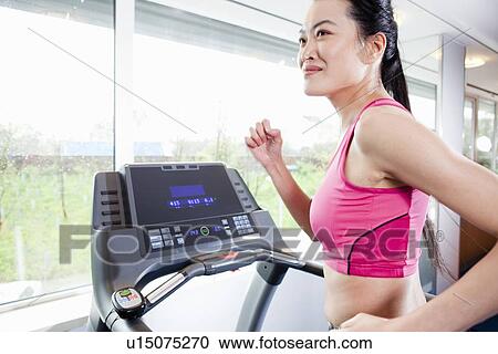 Stock Image - Woman running on treadmill in gym. Fotosearch