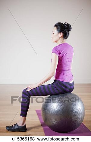 Stock Photo - Woman sitting on ball in yoga studio. Fotosearch
