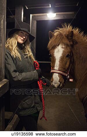 Stock Photo - Woman smiling with horse in stable. Fotosearch