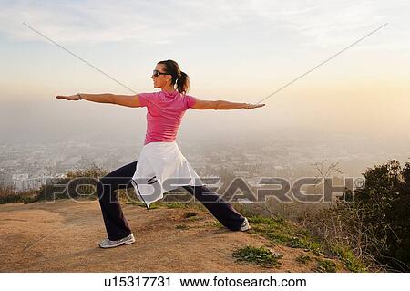 Stock Image - Woman stretching on hilltop. Fotosearch
